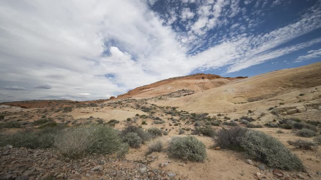 An ultrawide timelapse looking past sandy areas towards a steep white dome of rock in Valley of Fire State Park in Nevada.