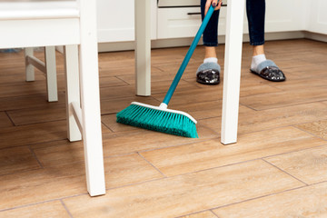 people, housework, cleaning and housekeeping concept - close up of woman legs with broom sweeping...