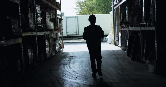 Silhouette of engineer walking between shelves in a warehouse to entrance