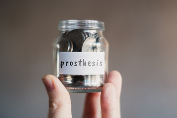Prosthesis savings concept - Glass jar with coins and inscription.