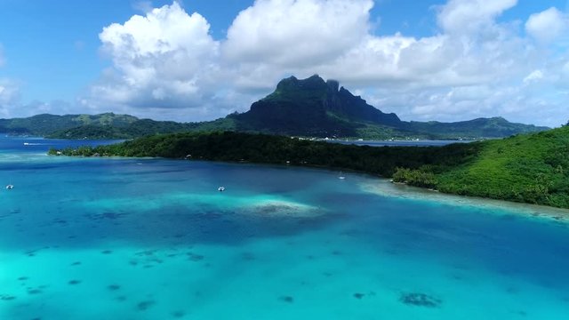 Gorgeous drone shot flying toward the amazing tropical landscape of honeymoon destination island Bora Bora, French Polynesia. Scenic Mountain peaks overlook the turquoise blue water of south pacific