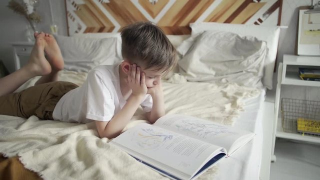 Teenage boy lays on bed and reads a book