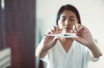 Woman hands holding a digital thermometer or measures the temperature at home