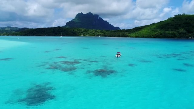 Beautiful drone shot of a speedboat in tropical island honeymoon destination island Bora Bora, French Polynesia. Boat floats in the blue turquoise water mountain peaks dot the coastline landscape