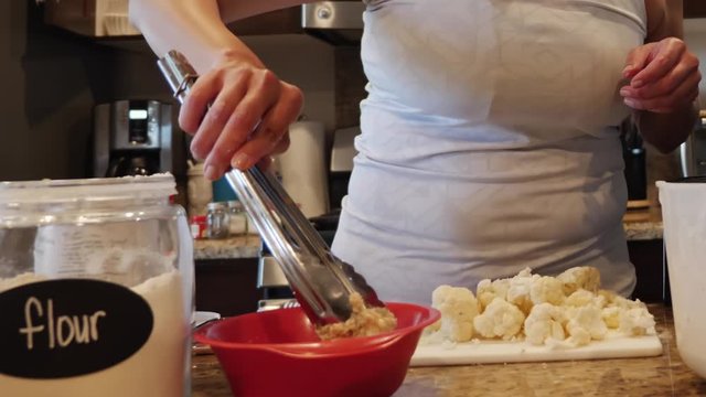 Woman chef dipping cauliflower into batter mix to prepare to cook