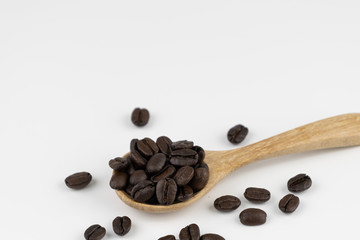 Roasted coffee beans on wooden spoon on white background