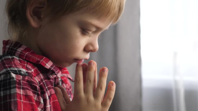 little son boy makes a wish prays bedtime religion concept. prayer child indoors praying by bed lifestyle in front of window