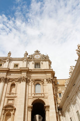 Statues of Christ and the Apostles and Oltramontano Clock on top of the facade of St Peter's Basilica with blue sky and clouds in Vatican City