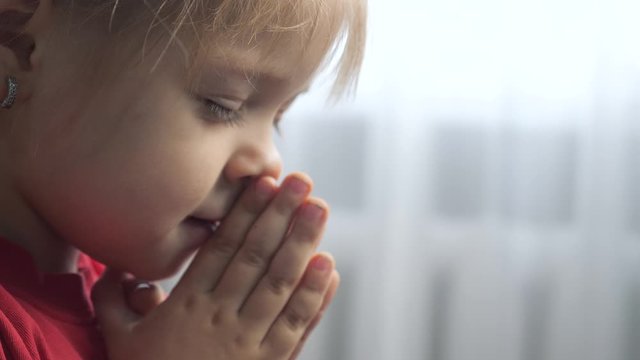 little daughter girl makes a wish prayers bedtime religion concept . prayer child lifestyle indoors praying by bed front of window