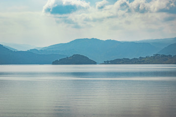 lake serene blue water with misty mountains and clouds reflections