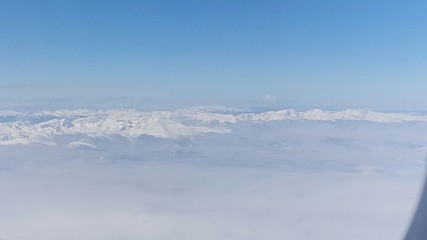Fototapeta na wymiar Aerial View Of Snowcapped Mountains In Clouds Seen From Airplane Window