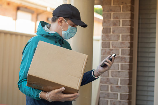 Contactless delivery during COVID-19 pandemic lockdown concept. Courier wearing mask and gloves holds a parcel box and checking address details on the smartphone