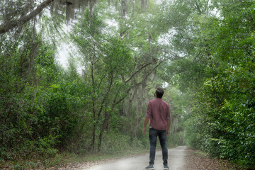 young man with brown hair and beard wearing red button down breathes in a breath of fresh air immersing himself in a nature path to social distance himself in order to stay healthy and alive.