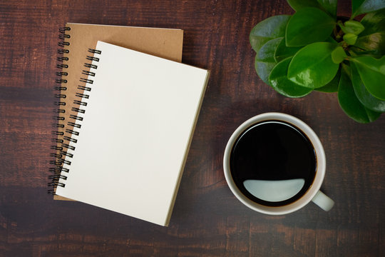 Top view of open school notebook with blank pages, Plant and Coffee cup on wooden table background. Business, office or education concept with copy space.