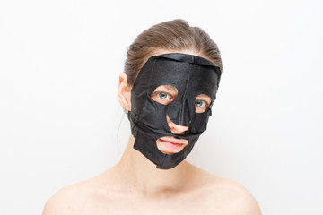 Portrait of a beautiful young girl with a black charcoal face mask.