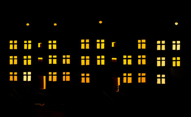 Silhouette of a three-story residential building with luminous windows