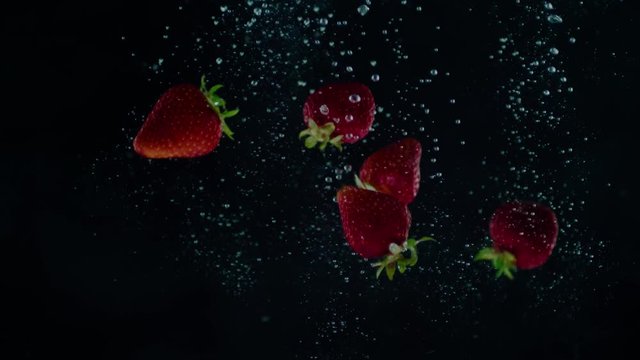 Strawberries falling into water with gradual slow motion applied.