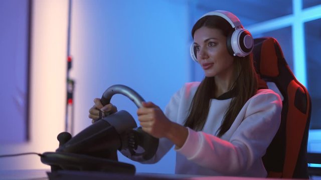 The attractive gamer girl with headphones plays games in the blue light room