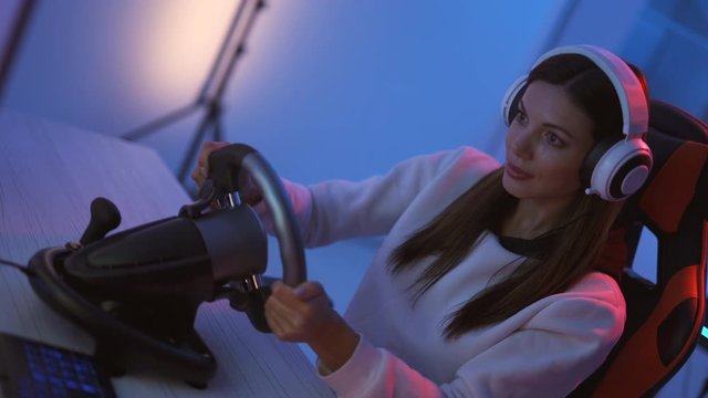 The gamer girl plays video games with steering wheel in the blue light room