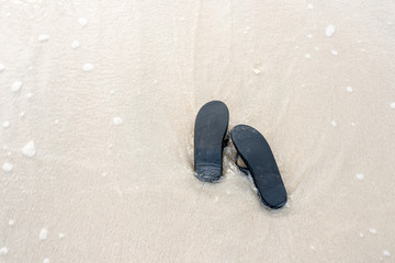 Fototapeta na wymiar Black slippers on the beach touched by waves from the sea.