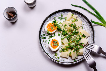 Boiled potatoes with herbs and soft-boiled eggs in a plate on grey concrete background. Selective focus