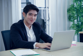 Portrait of asian smart young handsome businessman smiling at the camera and sitting at his desk in the office