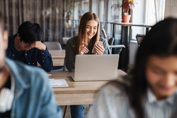 Photo of multinational young students using laptop and smartphone