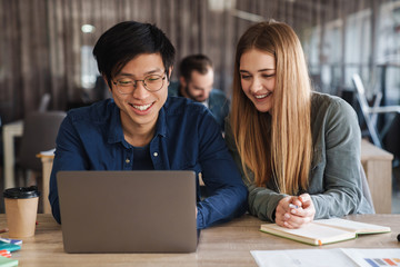 Photo of multinational cheerful students using laptop and laughing