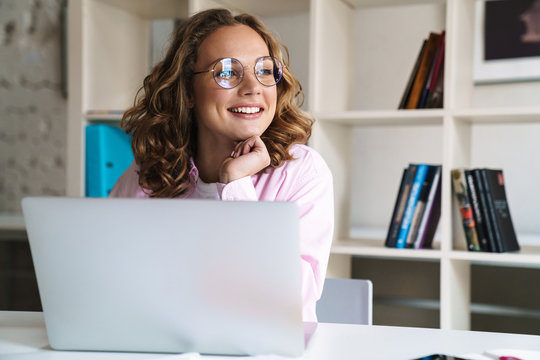 Photo of joyful woman wearing eyeglasses smiling and using laptop