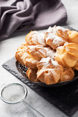 Profiteroles with custard and powdered sugar on a plate. Concrete grey table. Copy space.