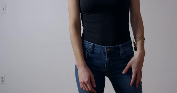 Attractive woman in black shirt and jeans dancing against white wall