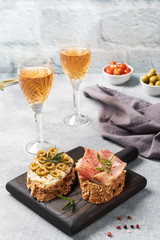 Wholegrain bread sandwiches with cream cheese, bacon and olives on a wooden cutting Board. A glass of white wine. Gray concrete background with Copy space.