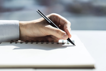Man writes with a pen in notepad in a sunny office, business and education concept. Close up