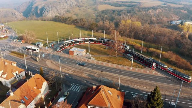 Aerial drone view of Tram arriving at terminal stop loop in Prague's District six at golden hour in natural park sarka lysolaje next to big road. sustainability and transportation concept