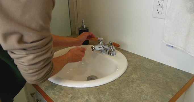 Medium shot of a man walking up to a bathroom sink and washing his hands.