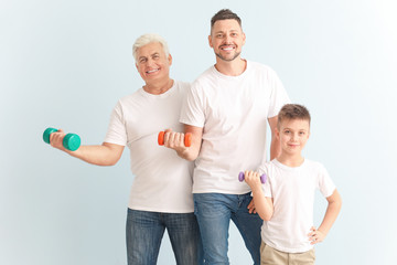 Man with his father and son holding dumbbells on color background
