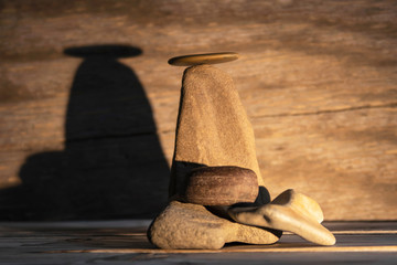 A figure made of stones on a wooden background, illuminated by light and creating a shadow.