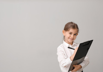 Little businesswoman with clipboard on grey background