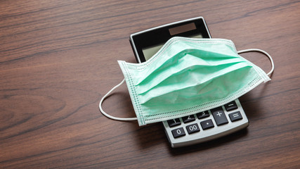 Protective mask on calculator on wooden table. Business financial impact of coronavirus pandemic...