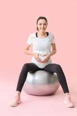 Young pregnant woman doing exercises with fitball on color background