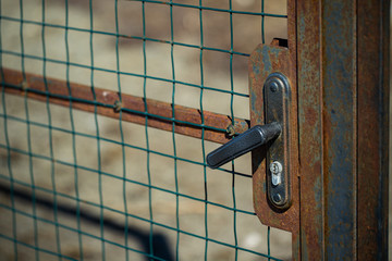 Rusty door, gate closed on a handle-lock with a metal mesh on the street
