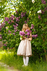 Obraz na płótnie Canvas kid girl in a pink dress near a lilac flowers 