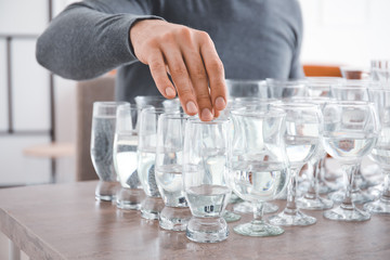 Young man playing music on glasses with water at home, closeup