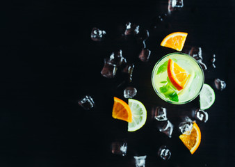 top of view of glass with cocktail and ice with lime and orange slice on black background