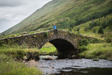 Traveller is sitting on a bridge in Scotland and enjoys the view