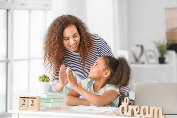Little African-American girl and her mother giving high-five to each other while doing homework in...