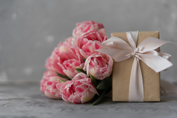 Close-up of a bouquet of cut pink lilac tulips with a craft gift box on a gray background.