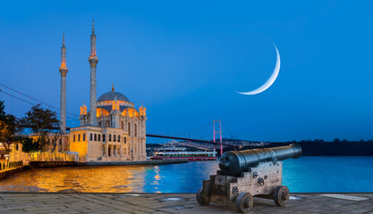 Obraz premium Ramadan Concept - Ortakoy mosque and Bosphorus bridge with crescent and cannon at twilight blue hour - Istanbul, Turkey