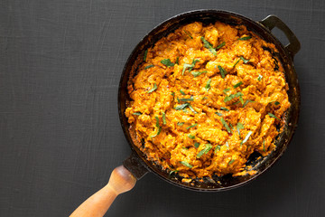 Homemade Chicken Tikka Masala in a cast iron pan on a black surface, top view. Flat lay, overhead, from above. Copy space.