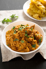 Homemade Chicken Tikka Masala in a white bowl on a black surface, side view. Flat lay, overhead, from above. Close-up.